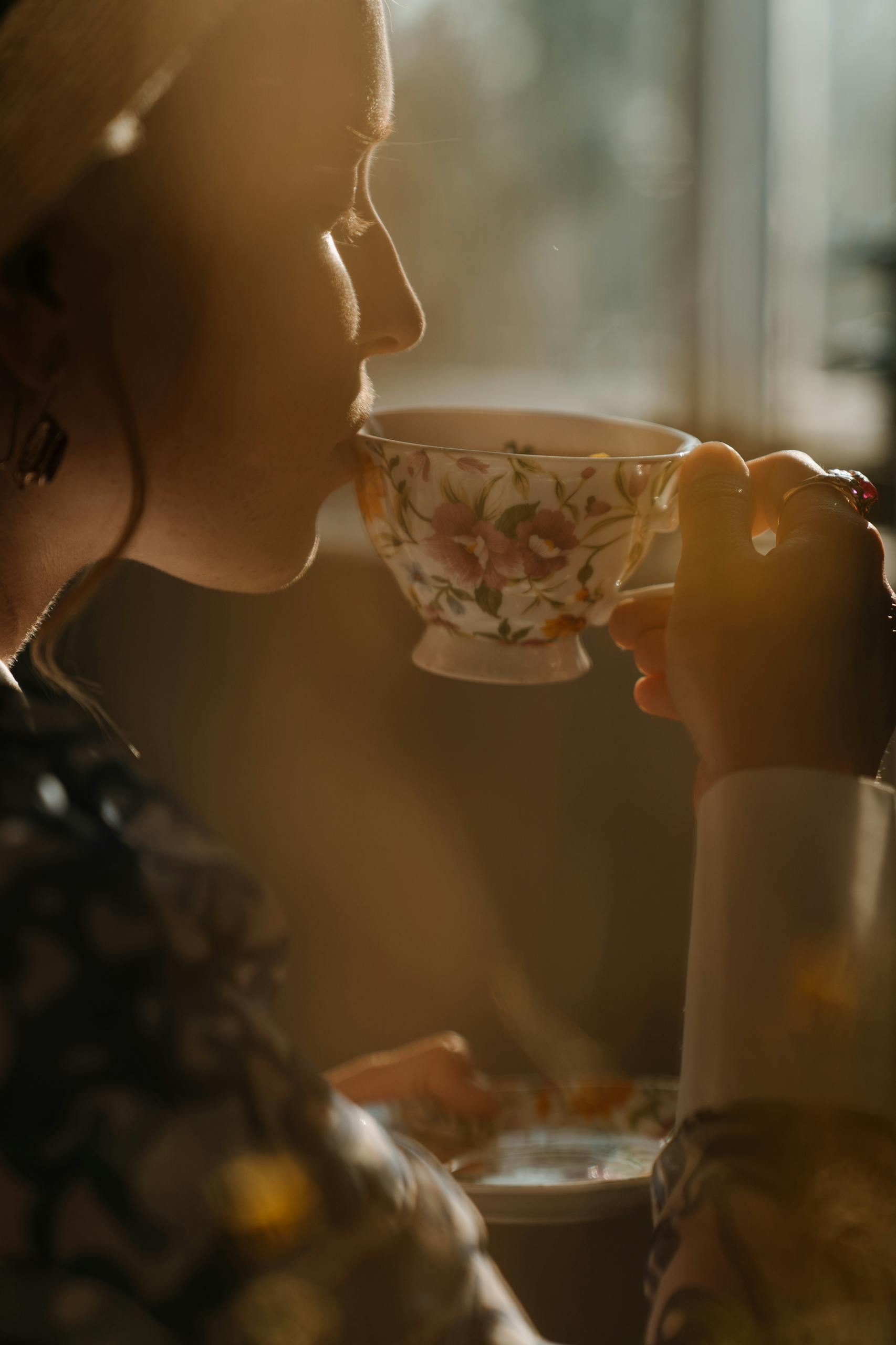 A woman sipping tea from a porcelain cup in a warm, softly lit setting, highlighting elegance and tranquility.