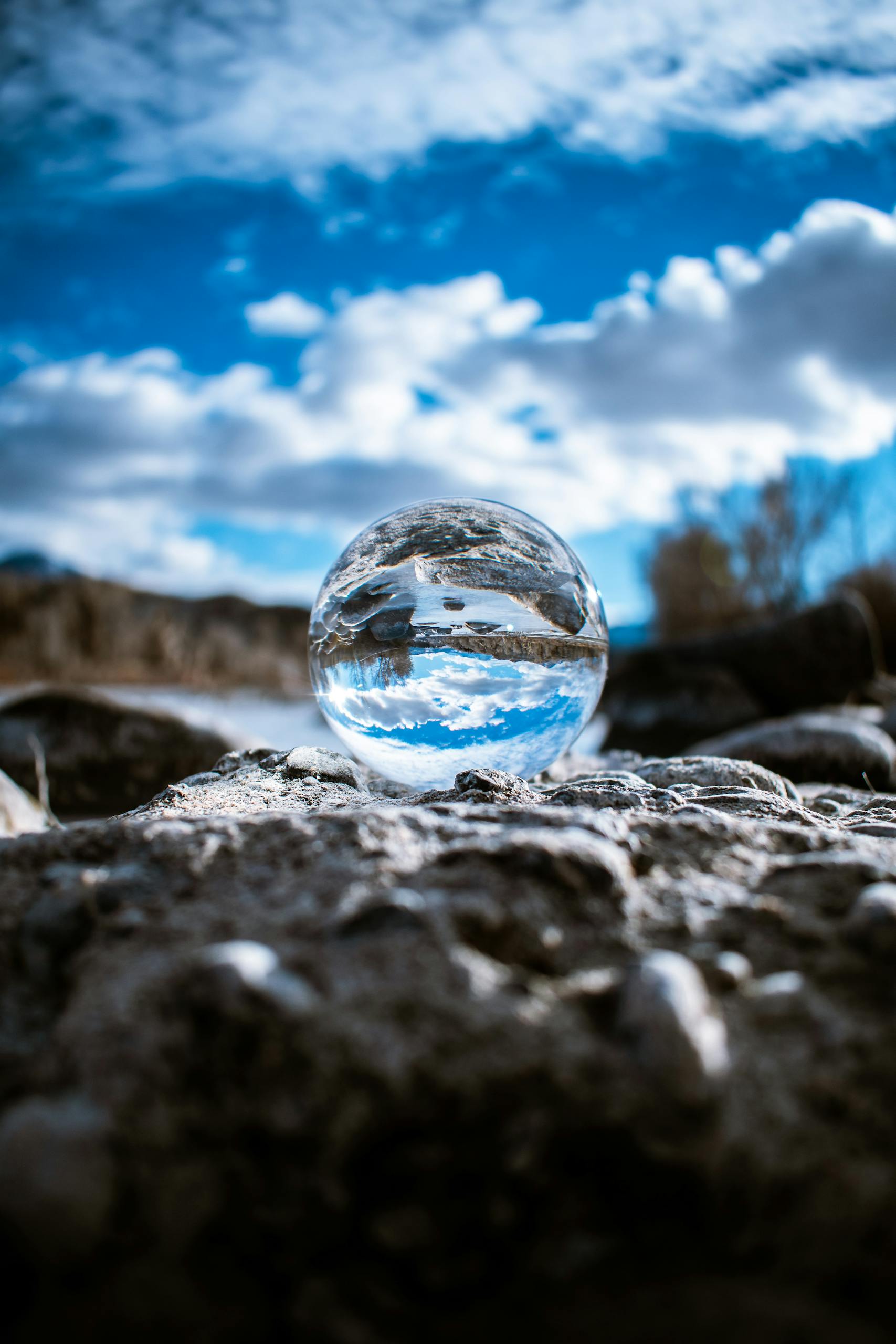 A crystal ball reflecting the sky and clouds creates a mesmerizing scene on rough terrain.