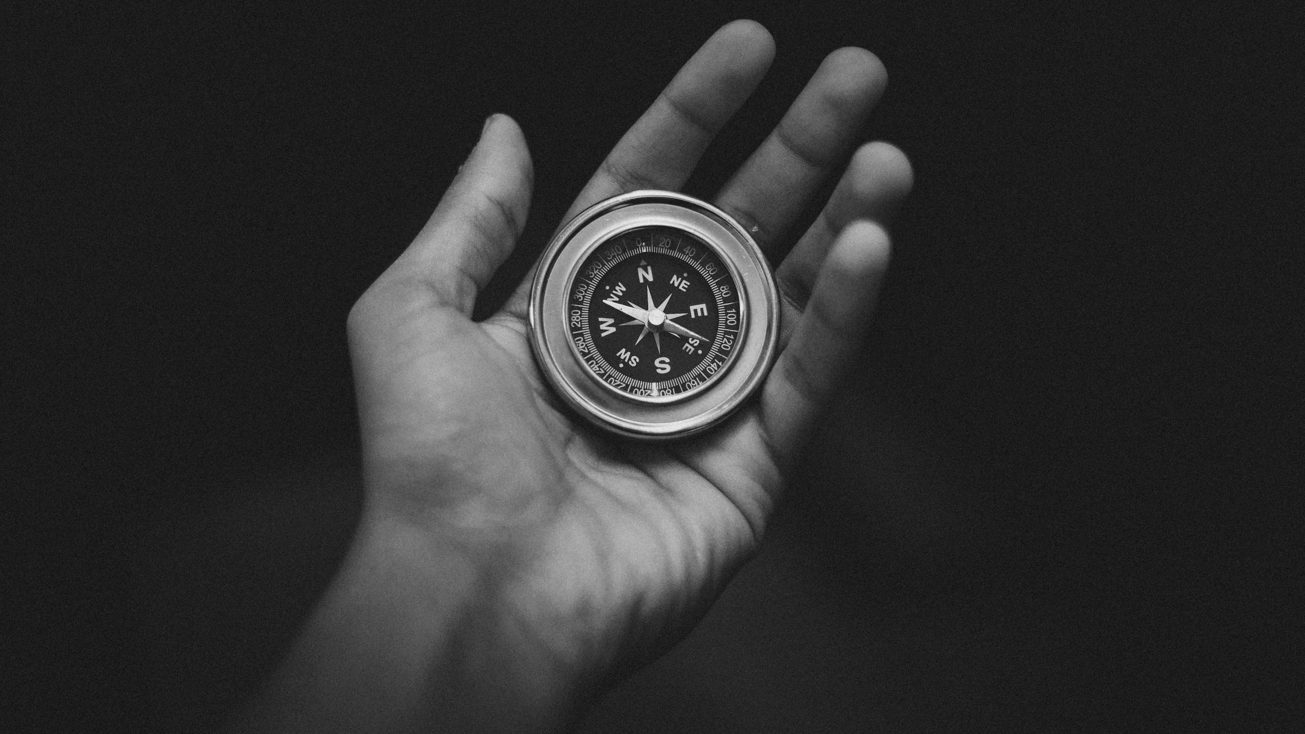 Black and white image of a hand holding a compass, conveying direction and exploration.